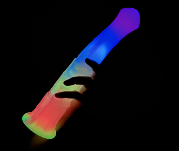 A big rainbow-colored horse dildo is held in a hand against a dark background. The dildo glows in different colors.