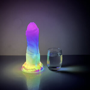 A bright, glowing dildo beside a clear glass of water, adding a playful touch to the setting.