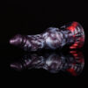 A knotted fantasy dragon dildo resting on a black and reflecting surface. The dildo is black and red.