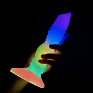 A hand holding a vibrant dildo against a dark background, showcasing its colorful design and glow.