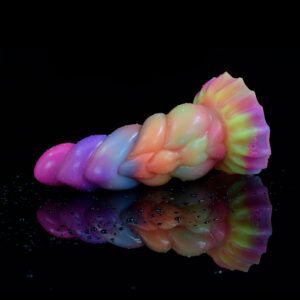 A vibrant and colorful fantasy dildo, laying on a black shimmering surface with water drops on it.