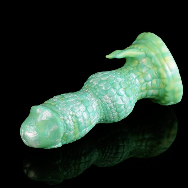 A green fantasy dildo resting on a black surface. The shaft features two big knots and a textures shaft that reminds of a snake skin.