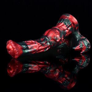 A fantasy dildo resting in front of a black background. The dildo features a big tip and balls with horns on them. The color of this dildo is black and red.