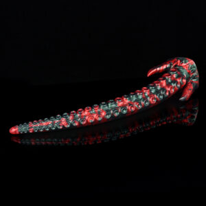 A black and red tentacle dildo laying on a black surface. The dildo features a long tentacle with small suction cups on it. The base of this fantasy dildo has two horns for external stimulation.